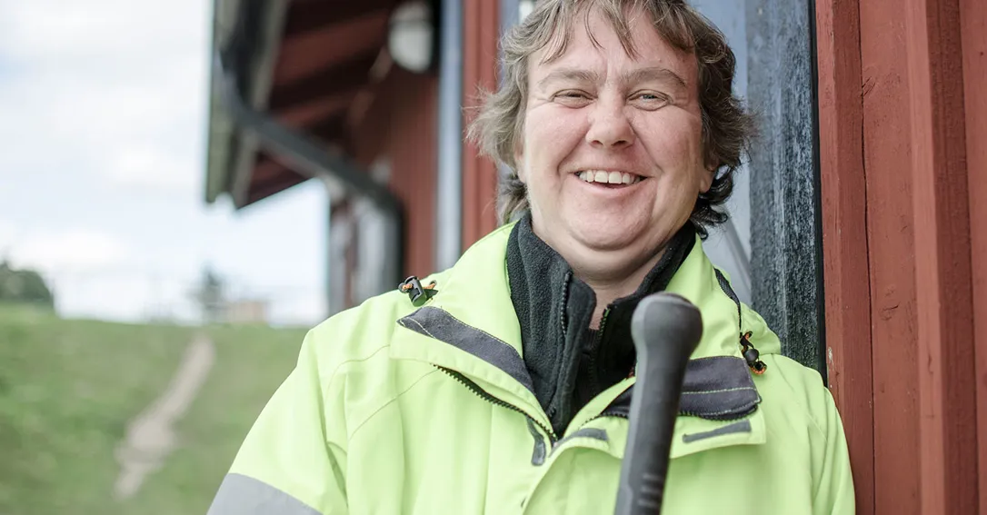 Bild på en glad kille som står utomhus mot en röd husvägg. Han bär reflexjacka och ler.