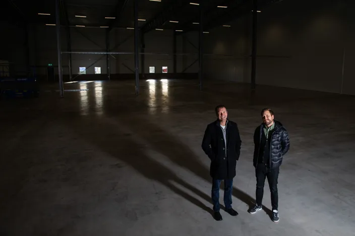 Två personer i nedsläckt lokal. Tittar in i kameran från ett fågelperspektiv. 