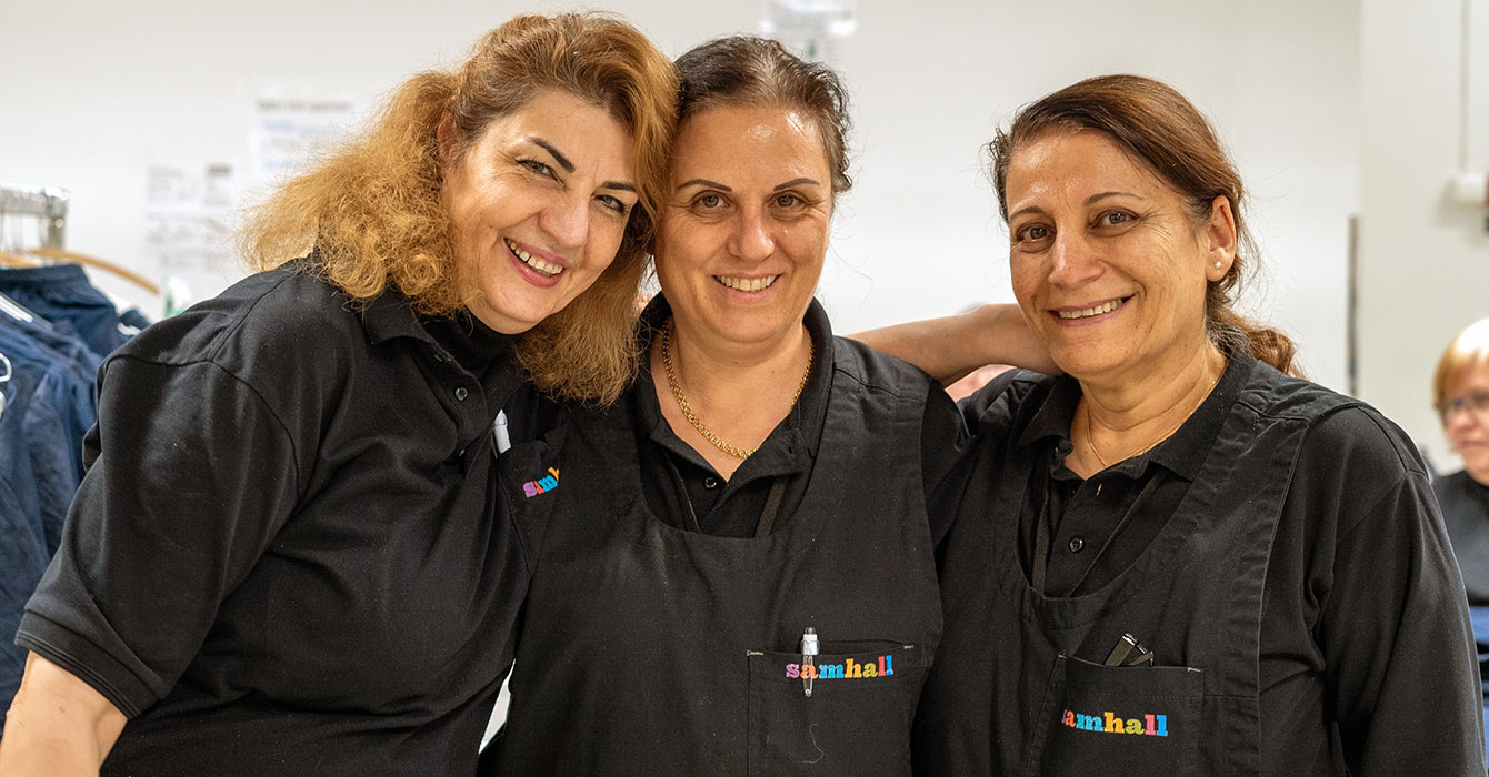 Tre personer ler och tittar in i kameran. De bär svarta arbetskläder.