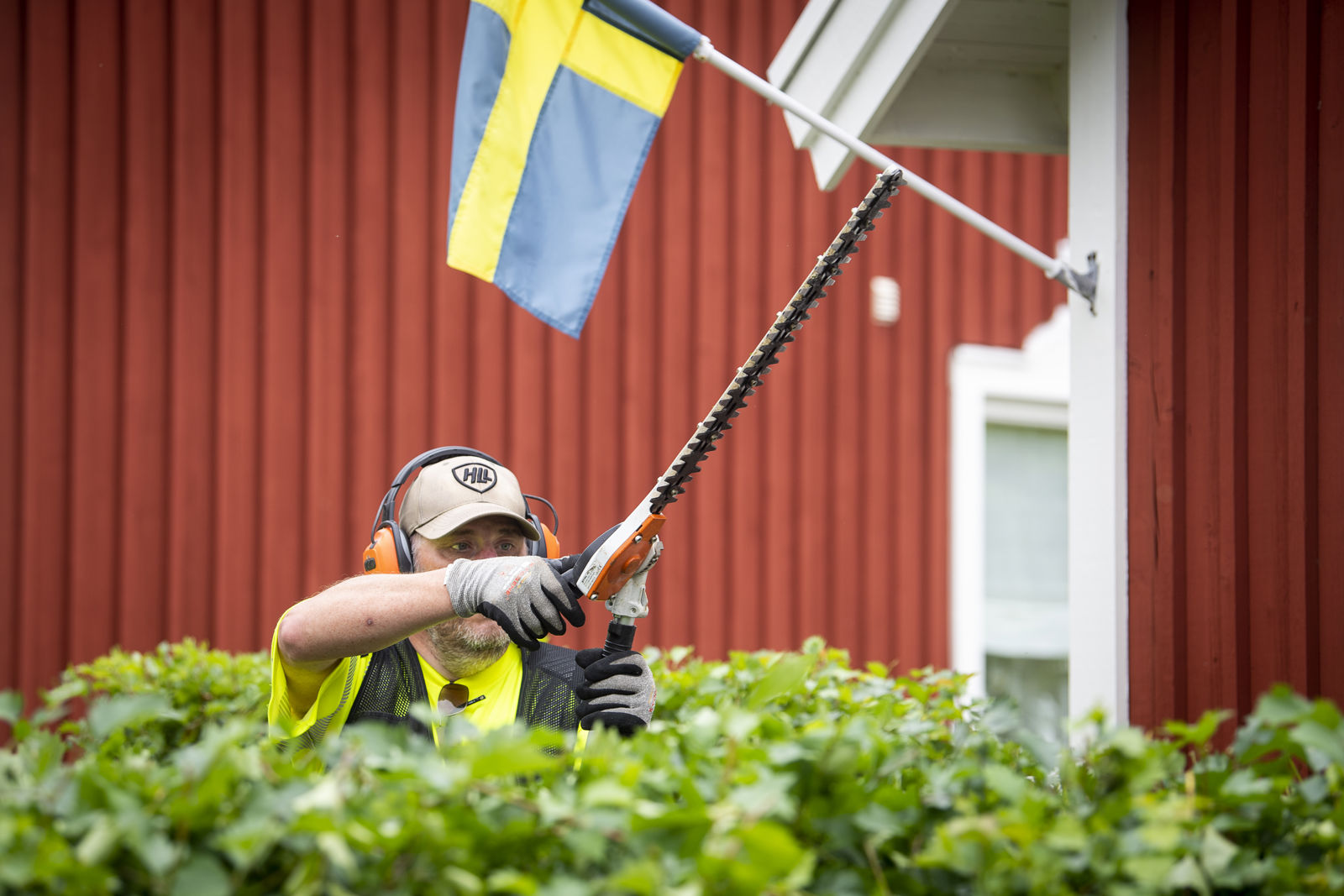 En samhallsanställd med trädgårdssåg framför en röd byggnad.