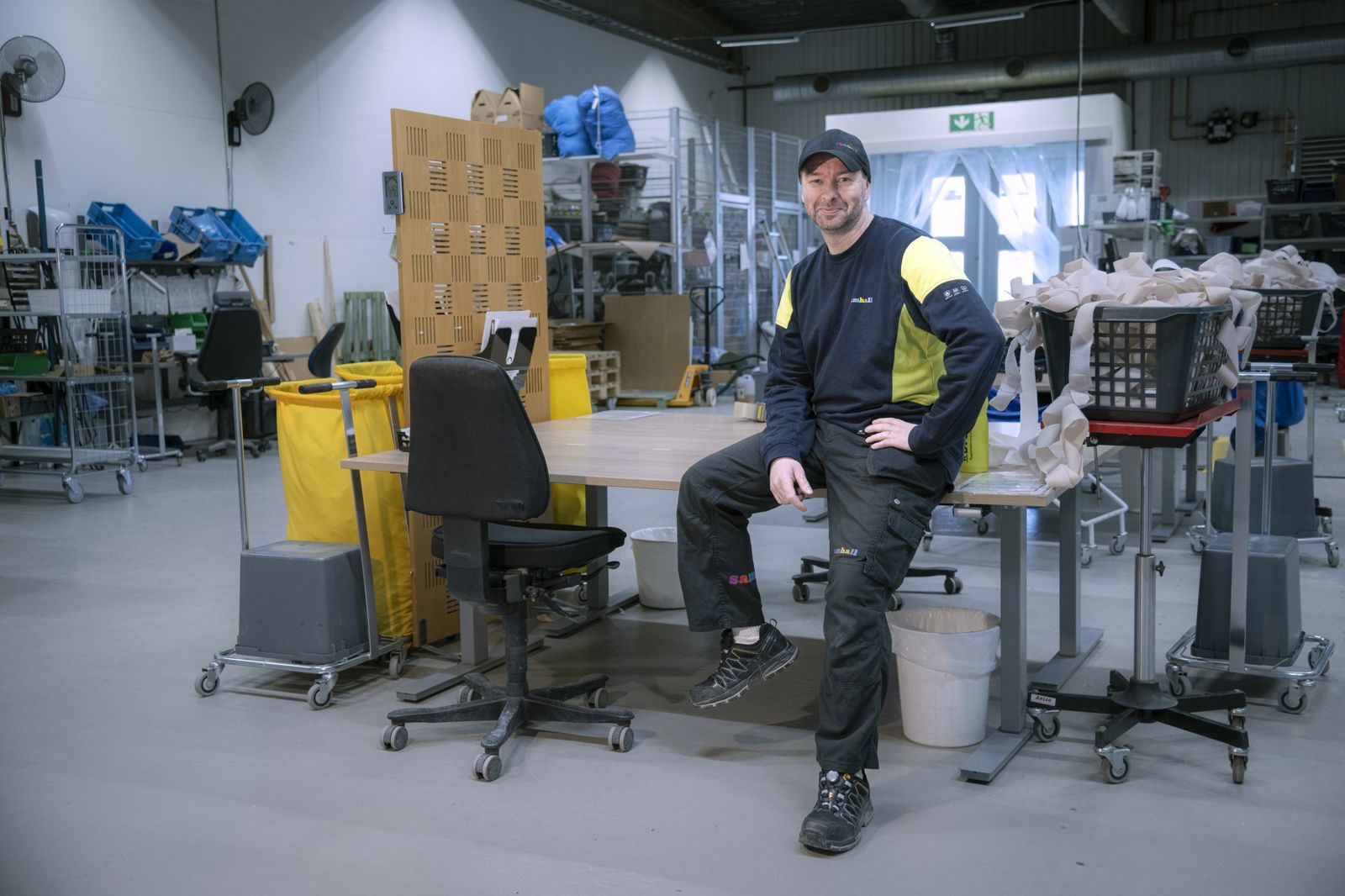 Man som sitter på skrivbord, han ler och tittar in i kameran. Han har en keps på huvudet.