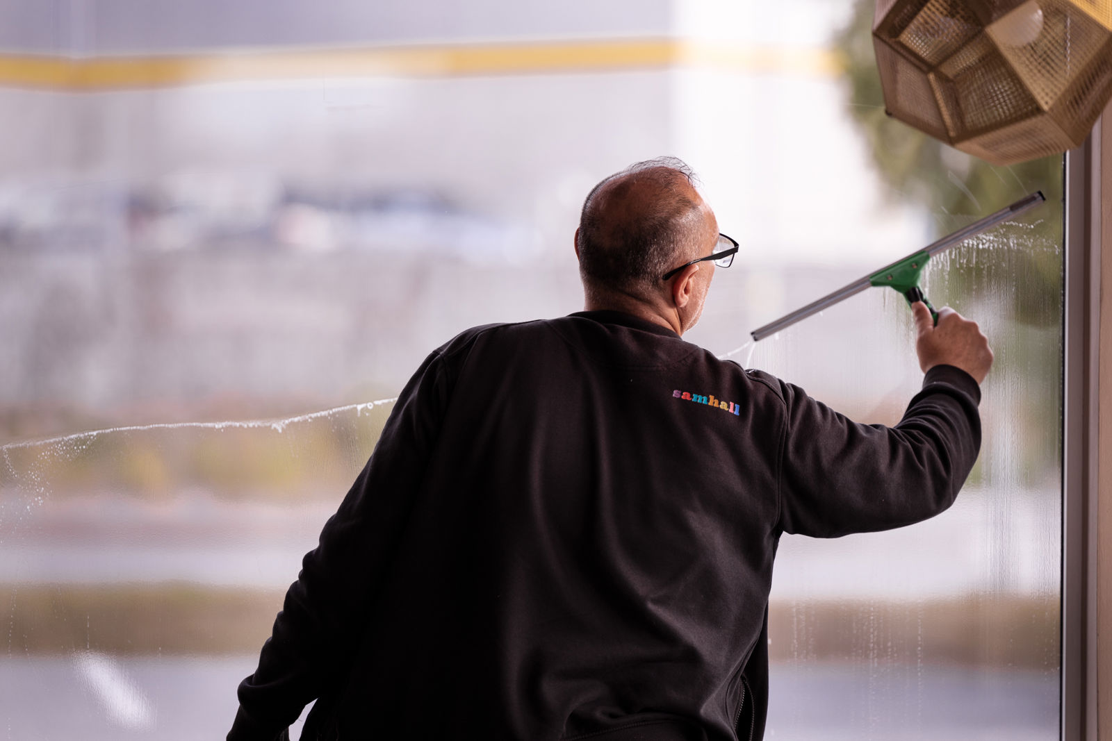  En samhallmedarbetare putsar ett fönster med en fönsterputs.