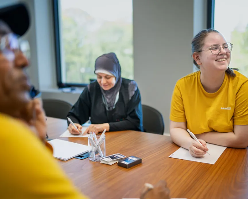 Medarbetare sitter runt ett bord i ett möte och antecknar medan de lyssnar.