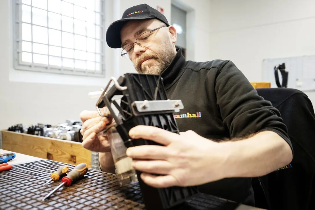 En Samhallmedarbetare monterar en komponent vid en arbetsstation med verktyg.