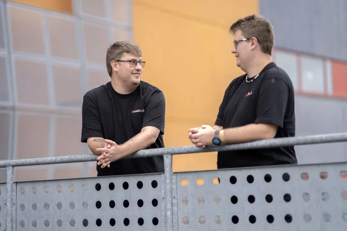 Pontus och Linus står lutade över ett metallräcke. Bakgrunden är orange. 