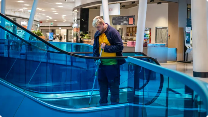 En Samhallmedarbetare rengör en rulltrappa i en galleria.