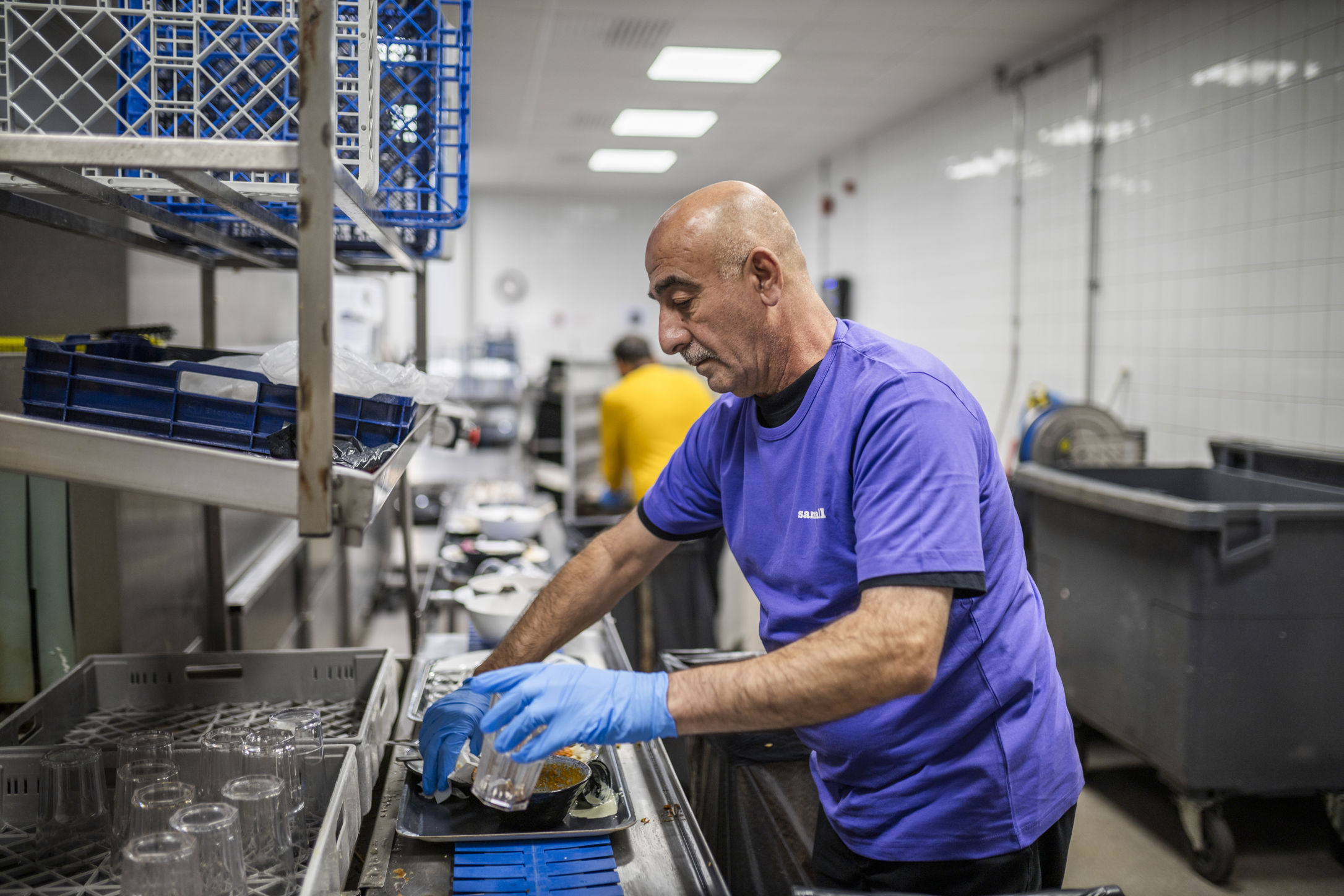 Samhallsmedarbetare arbetar i ett restaurangkök och diskar glas och tallrikar vid en disklinje.