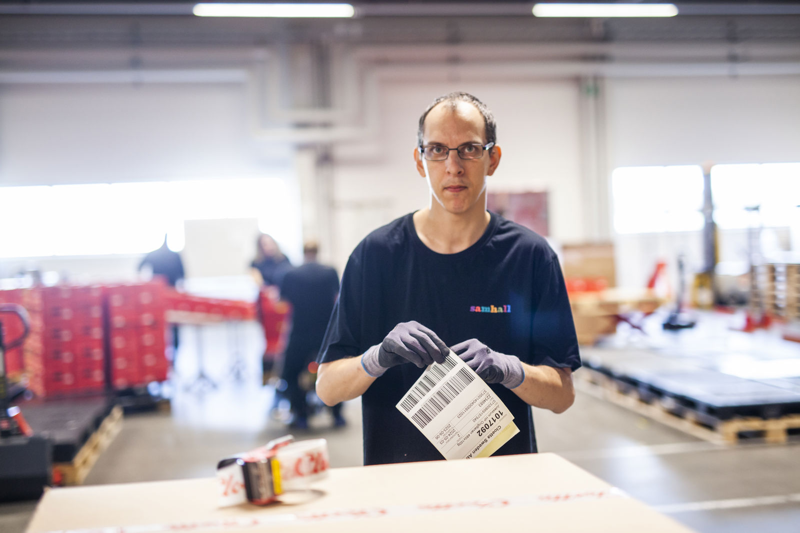 En samhallsanställd i en lagerlokal med ett papper i handen.