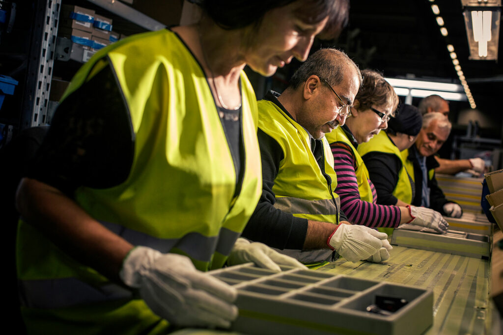 Samhallsmedarbetare arbetar tillsammans vid ett produktionsband i industrimiljö.