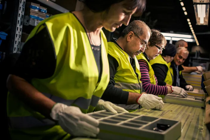 Samhallsmedarbetare arbetar tillsammans vid ett produktionsband i industrimiljö.