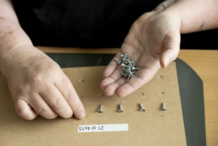 Bild på händer som arbetar med skruvar. Den ena handen håller i dem och den andra placerar dem på bordet. 