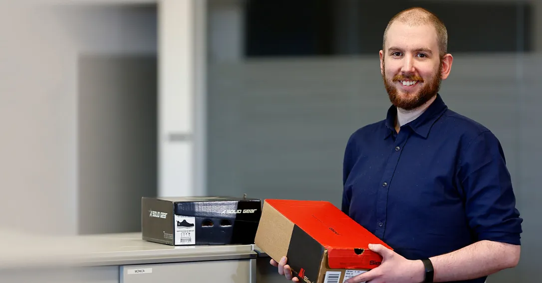 Bild på en man som bär mörkblå skjorta och håller i en röd låda.