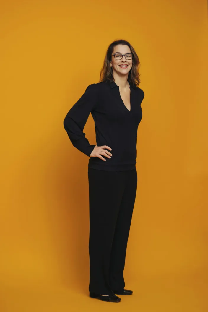 Porträtt av Sara Revell Ford framför en orange fondvägg. Hon syns i helkropp. 