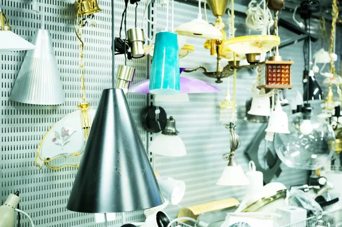 Flera olika taklampor och armaturer hänger tätt bredvid varandra i en butiksmiljö. Lamporna har varierande former, färger och material, från metalliska konformade skärmar till glas- och plastkupor.