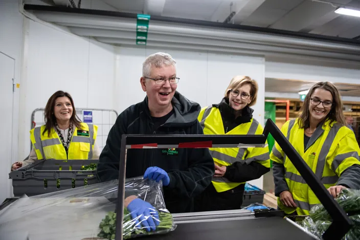 Bild på fyra personer som ler i en industrilokal. De bär alla arbetskläder i olika färger, bland annat svart och reflexfärg.  