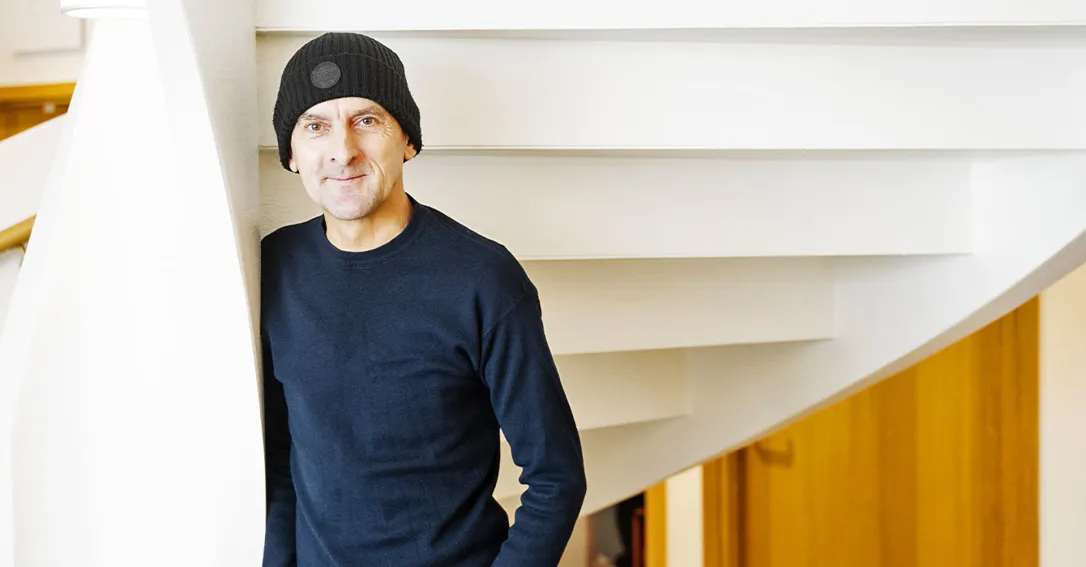 Bild på en man som står i en trappa och litar sig mot en vägg. han har mörka kläder och mössa.