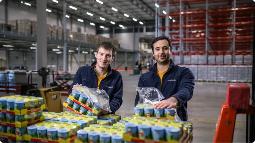 Två Samhallmedarbetare arbetar i en lagerlokal och hanterar förpackningar med varor.