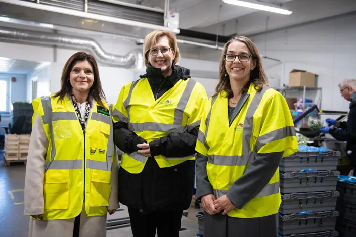 Bild på tre kvinnor i en industrilokal. De bär alla arbetskläder i  reflexfärg.