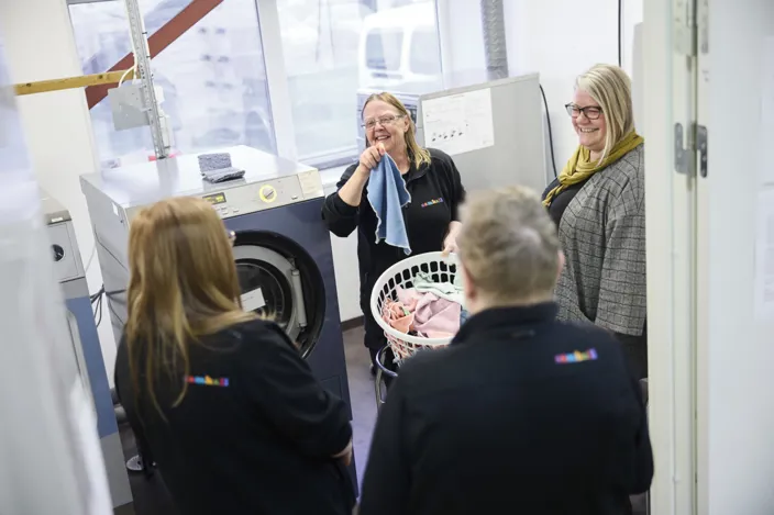 Bild på fyra personer som står i ett tvättrum. Två har ryggen vänd mot kameran och på ryggarna står det Samhall. 