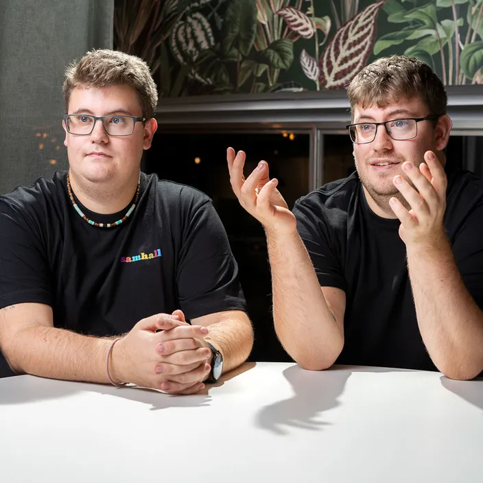 Bild på tvillingarna Linus och Pontus som sitter lutade över ett bord. De har båda två glasögon och bär svarta tröjor. 