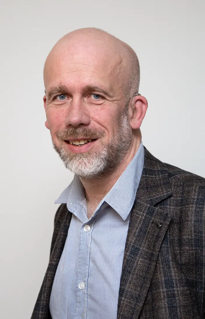 porträtt av man som bär blå skjorta och mörk kavaj. vit bakgrund. 