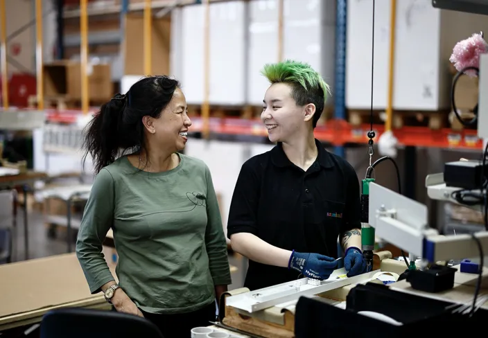 Bild på Tot Doung och Albert Bernhardsson, varav den sista har grönt hår och den förstnämnda svart hår. De står i en lagerlokal och tittar på varandra. 