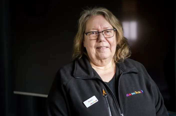 Porträtt av Annica Falck som bär svarta arbetskläder och glasögon. Bakgrunden är mörk. 