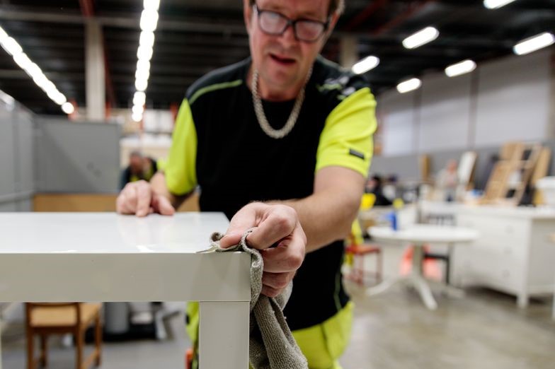 En person i arbetskläder putsar ett bord i närbild