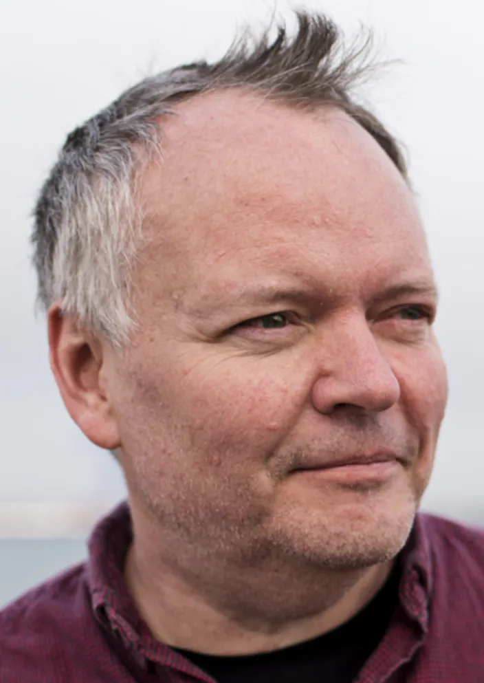 Bild på en man i profil som tittar åt sidan. Han har grått hår och en röd tröja.