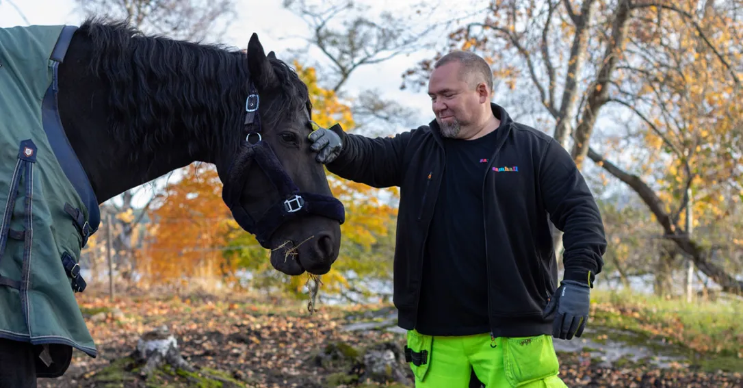 bild på en man som klappar en svar häst i ett höstligt skogslandskap.