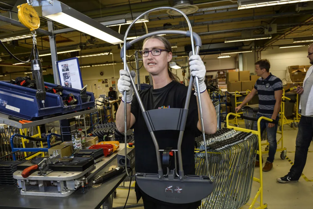 Person med långt hår i hästsvans och glasögon jobbar i ett rum.