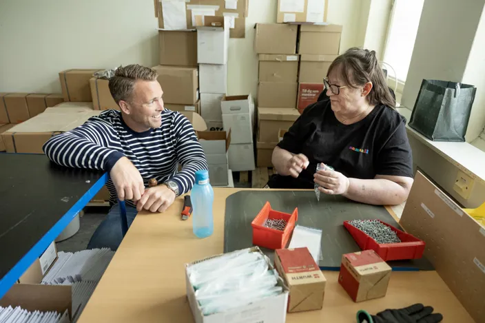 Bild på två personer som sitter bakom ett arbetsbord och pratar.