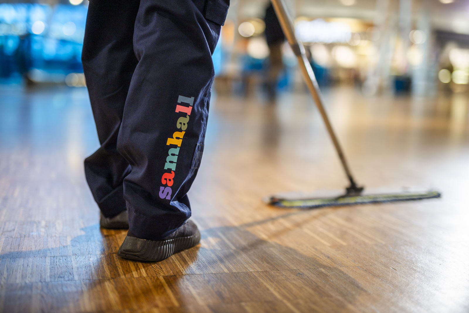  Detaljbild på ben/blå byxor med Samhall-logga. Personen skurar golv.