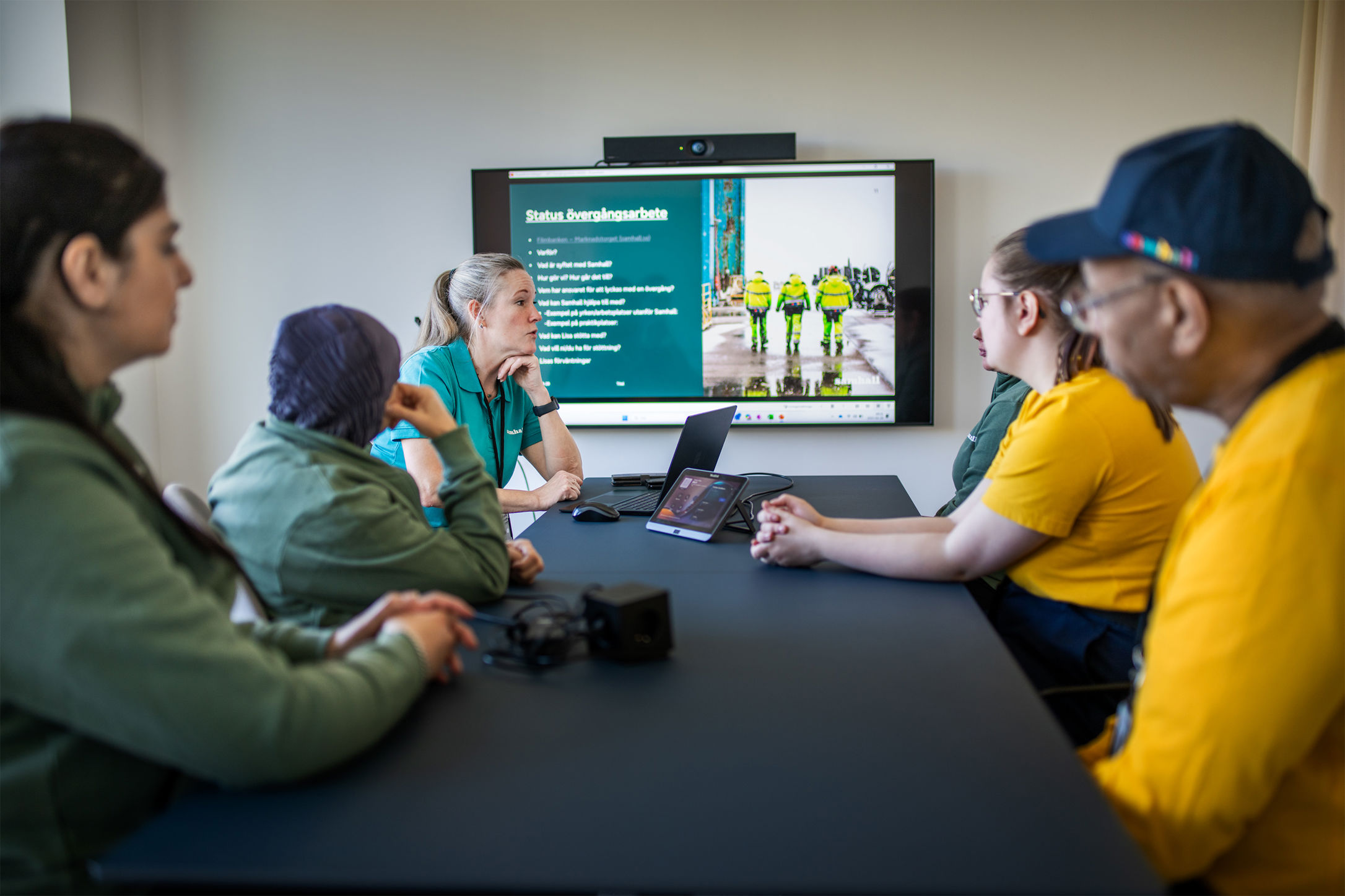 En grupp medarbetare deltar i ett möte där en presentation visas på en skärm i konferensrummet.