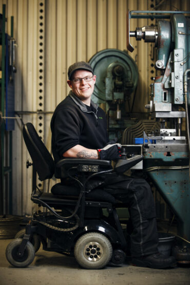En person i rullstol siter vid en maskin i en verkstad