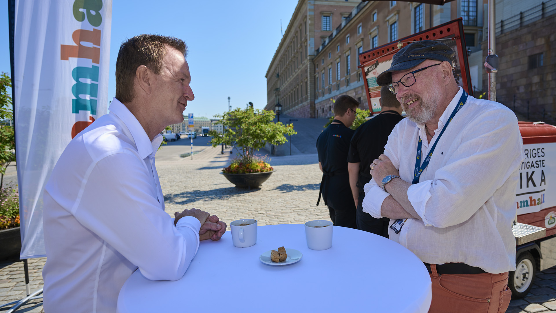 Två män i vita skjortor står runt ett bord ute