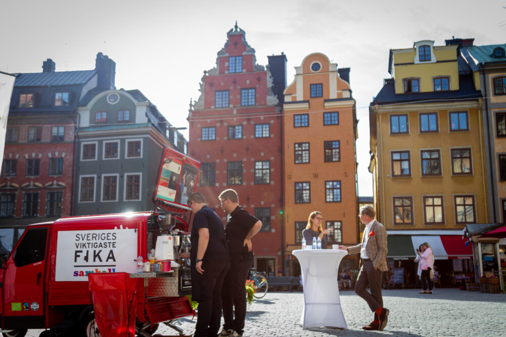 Ett kaffestånd i en röd liten bild ute på ett torg med människor i rörelse