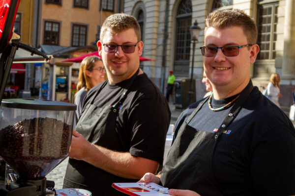 Bild på tvillingarna Pontus och Linus Nilsson som står och förbereder kaffe på ett torg i Stockholm. De bär svarta Samhall-tröjor.