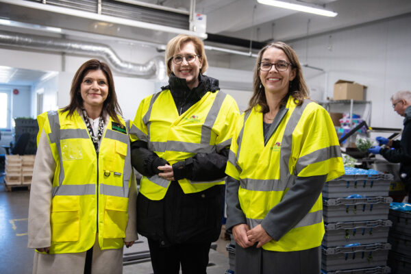 Bild på tre kvinnor i en industrilokal. De bär alla arbetskläder i  reflexfärg.