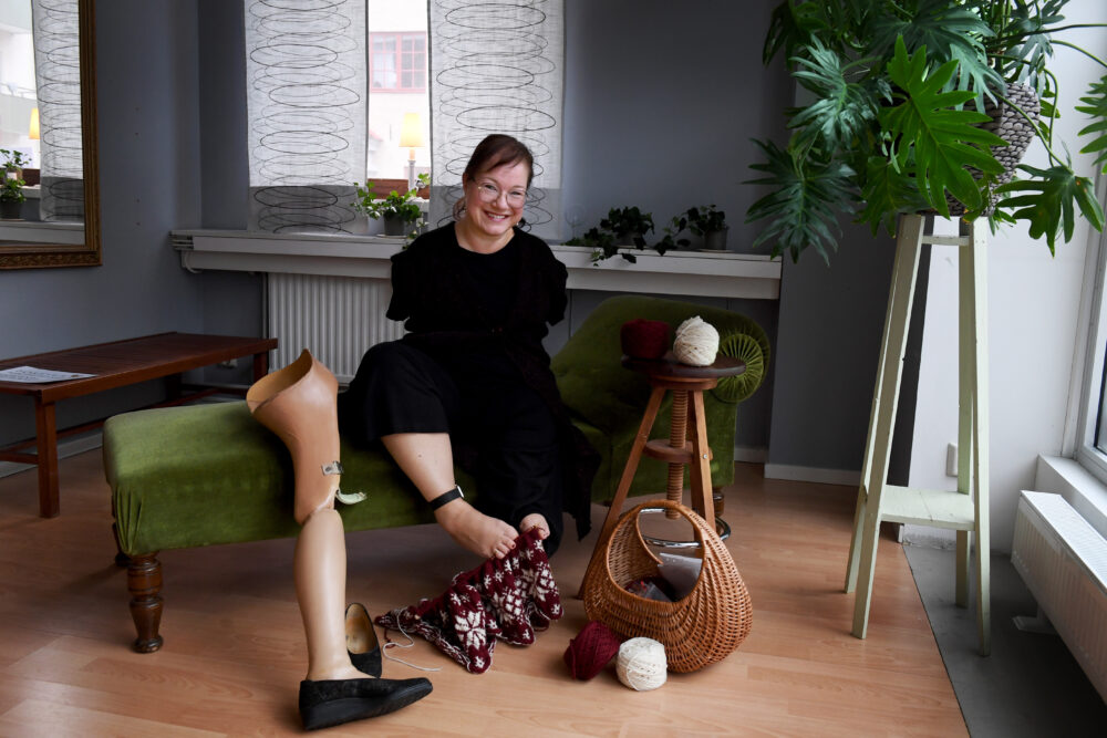 Lena Maria Vendelius sitter på en soffa och stickar med fötterna.