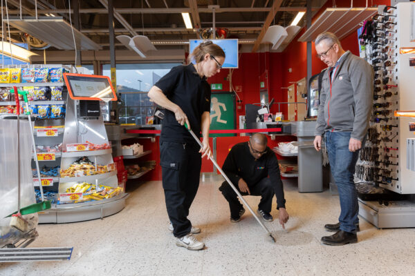 Samhall-medarbetarna Carola Granlöf, Lars Westerlund och Ica-handlaren Ulf Schön står och kontrollerar Carolas tvättning av golvet i ica-butiken.