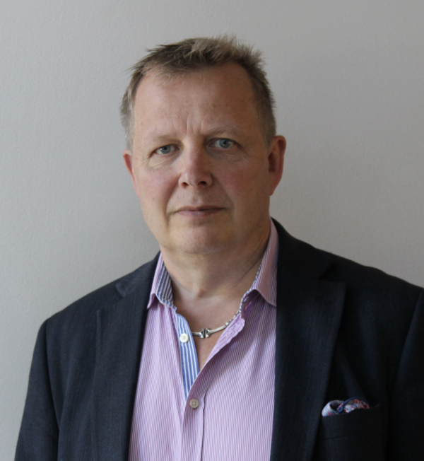 Porträtt av Jukka Lindberg. Han bär lila skjorta och svart kavaj. 