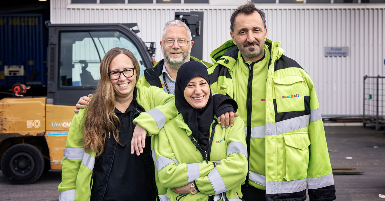 Fyra samhall-medarbetare står i grupp framför en truck, de bär arbetskläder med reflexfärg.