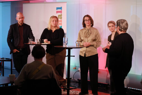 Bild på fyra paneldeltagare på en scen. En moderator står med ryggen ädn och ställer frågor till övriga deltagare.