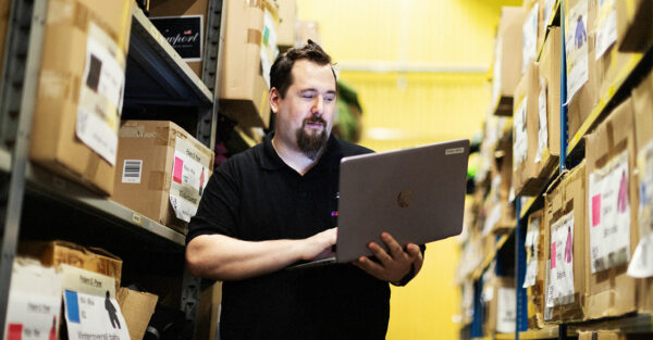Bild på Jimmy som står mellan två lagerhyllor och håller i en bärbar dator.