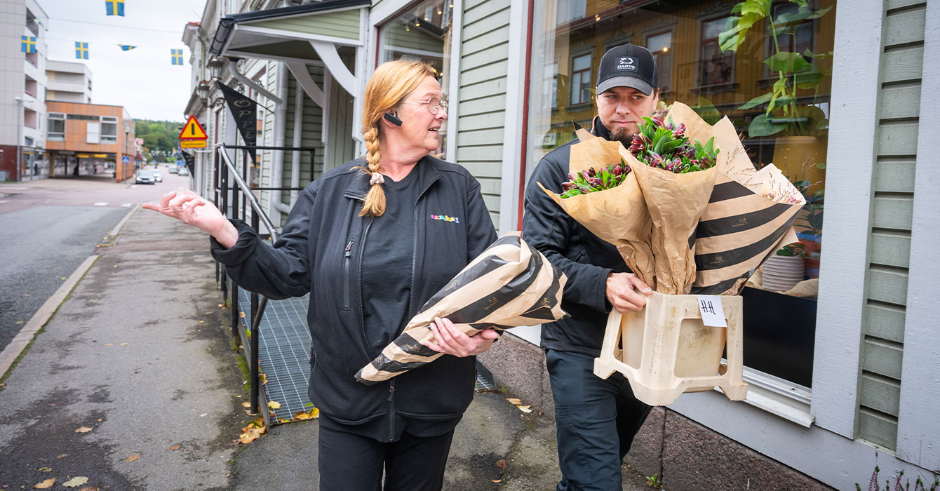 Bild på två personer som bär på blomsterbuketter på en innerstadsgata i Filipstad.