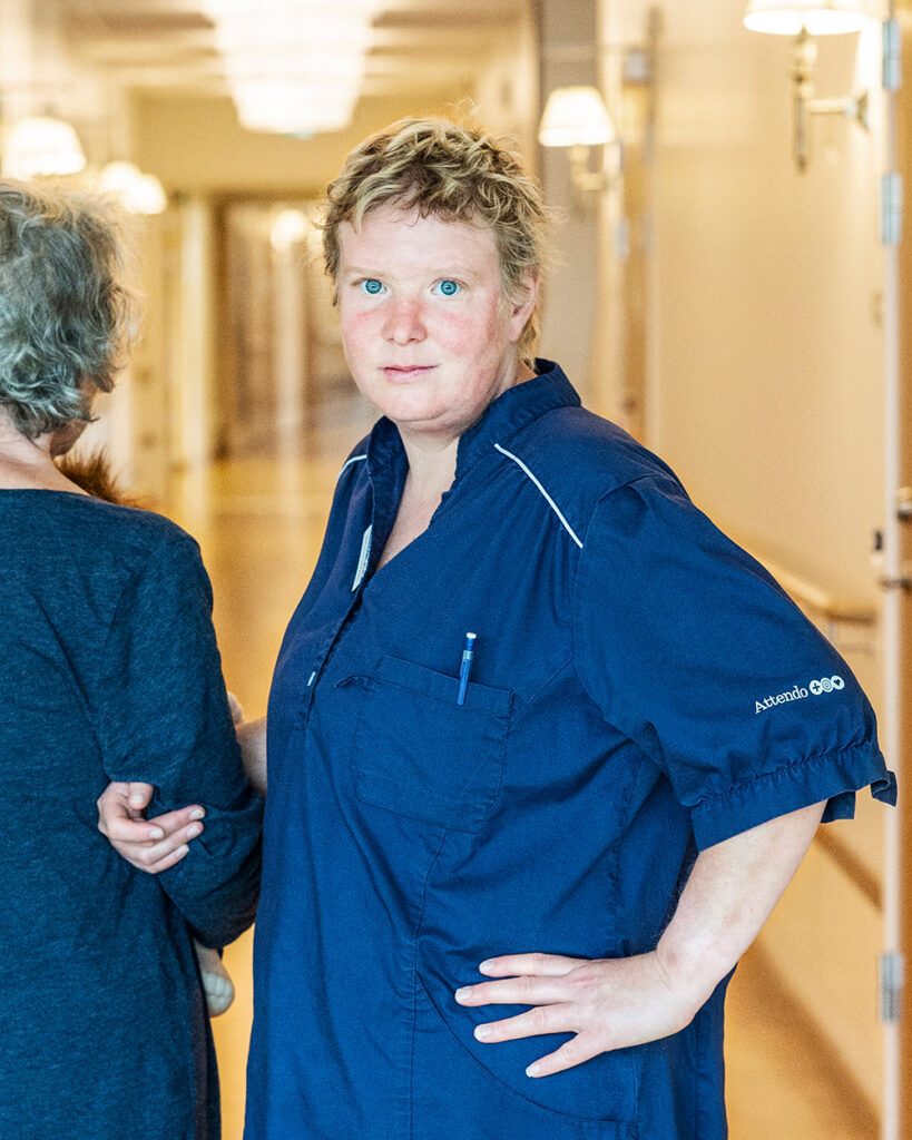 Person som jobbar inom äldrevården tittar in i kamran och håller armkrok med en vårdtagare.