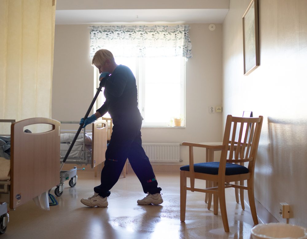 Kvinna i motljus som moppar golv i ett rum.