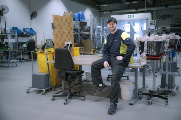 Man som sitter på skrivbord, han ler och tittar in i kameran. Han har en keps på huvudet.